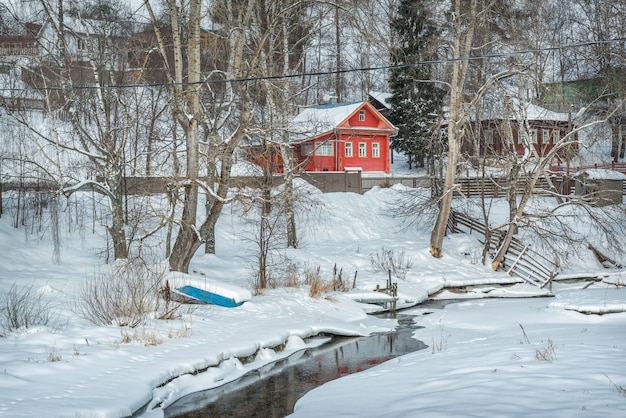 Edificio residencial rojo a orillas del río Shokhonka congelado en Plyos a la luz de un día de invierno bajo un cielo azul