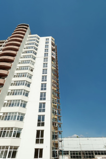 Edificio residencial de varios pisos en construcción y grúa sobre un fondo de cielo azul