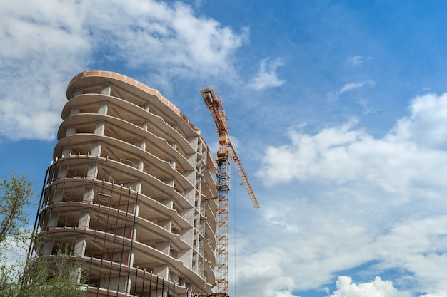 Edificio residencial de varios pisos en construcción y grúa sobre un fondo de cielo azul