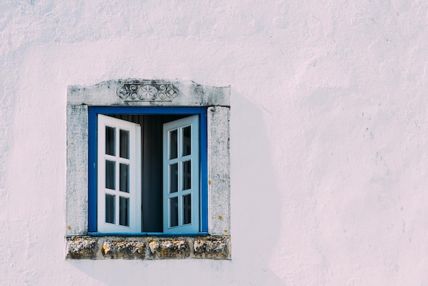 Edificio rosa con hermosa ventana blanco-azul con adornos en Obidos, Portugal