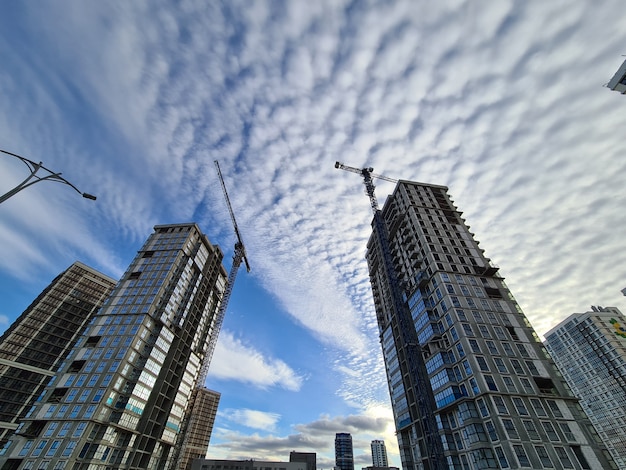 Edificios de varios pisos en construcción con grúas torre contra el fondo de cielo azul con nubes. Venta de concepto de apartamentos