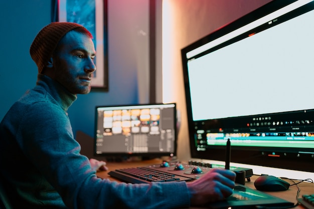 Foto editor de vídeo masculino atraente trabalha com filmagem ou vídeo em seu computador pessoal, ele trabalha no creative office studio ou em casa. luzes de neon