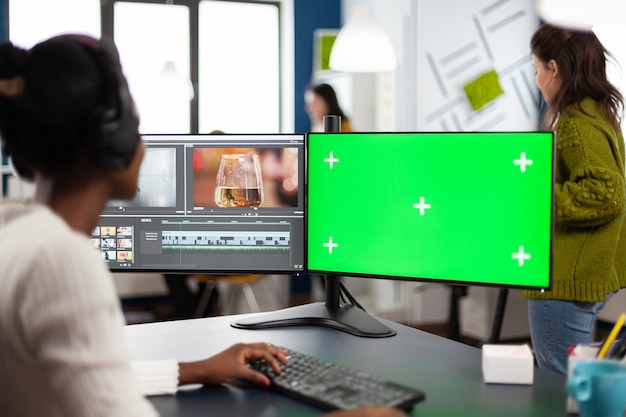 Editor de video de mujer negra desarrollando nuevo montaje de película de proyecto mirando pantalla verde, pantalla aislada de clave de croma de computadora, sentado en agencia creativa