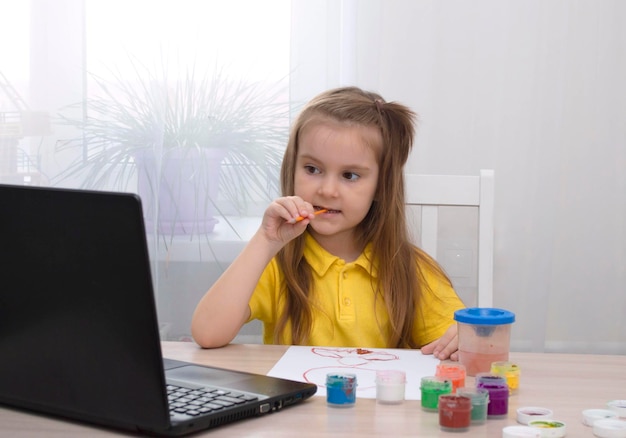 Educação a distância do conceito. A menina aprende a desenhar online durante o auto-isolamento. Estude online. Aula de desenho com laptop. Faça um desenho com cores. A vida na era digital. de volta à escola.