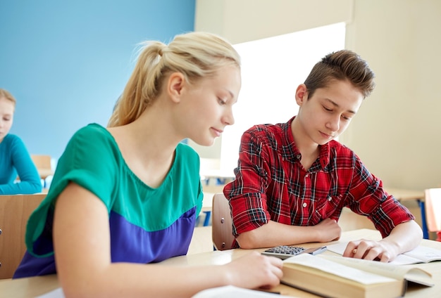 educação, aprendizagem e conceito de pessoas - alunos com livro e calculadora na aula escolar