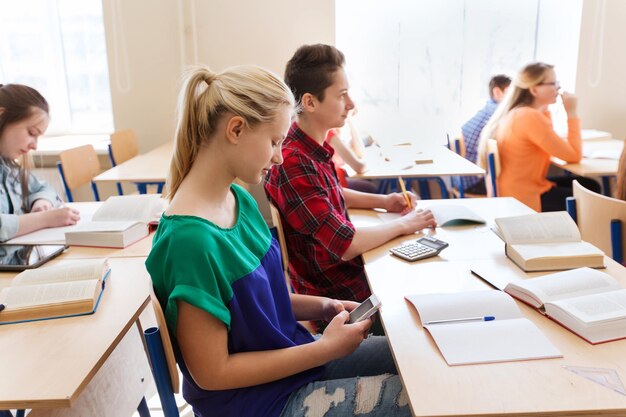 educação, aprendizagem, tecnologia, comunicação e conceito de pessoas - aluna com mensagens de smartphone na aula escolar