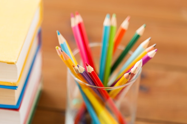 educação, arte, desenho, criatividade e conceito de objeto - close-up de giz de cera ou lápis de cor e livros sobre mesa de madeira