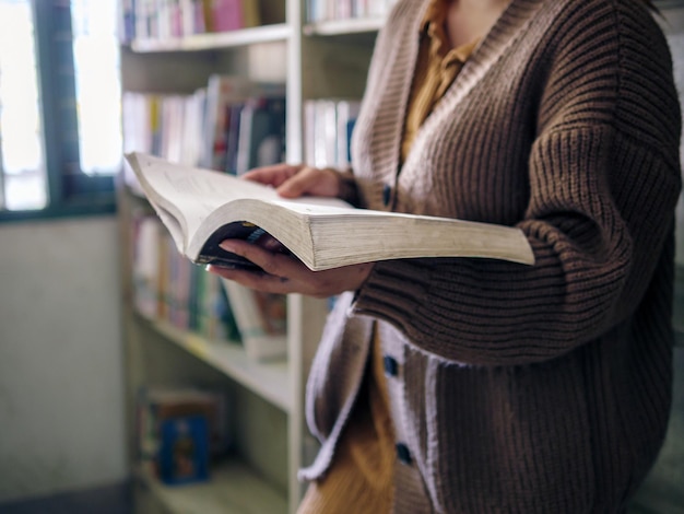 Foto educação de aprendizagem mão de mulher idosa de pé segurando um livro na biblioteca