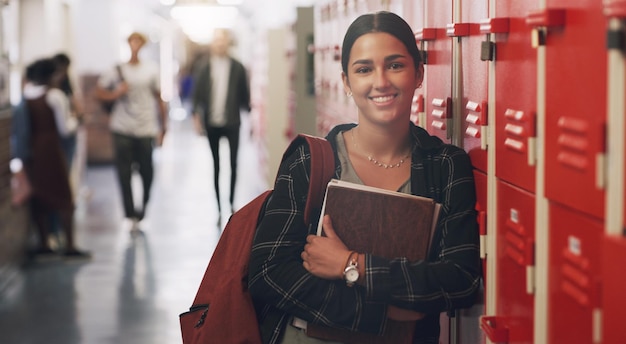 Educação de retrato e livros com uma aluna ao lado de seu armário no corredor de sua escola aprendendo universidade e bolsa de estudos com um aluno universitário segurando um caderno para estudar o conhecimento