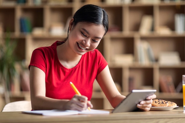 Educação em casa e novo aplicativo Jovem estudante asiática alegre fazendo lição de casa com tablet assistir aula on-line