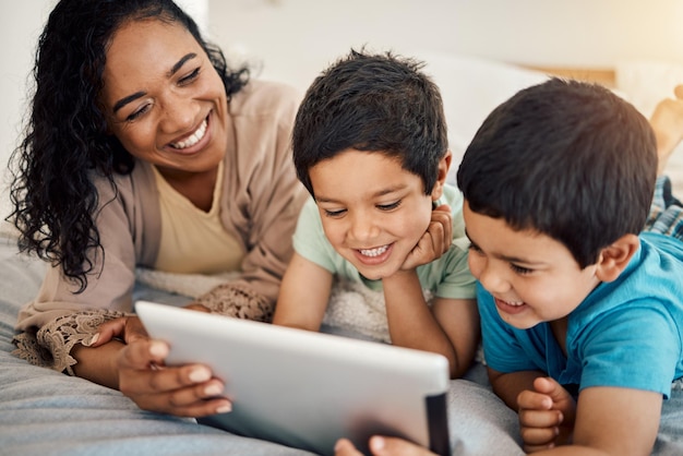 Educação em tablet e uma mulher com seus filhos em uma cama em casa pela manhã juntos para entretenimento Menino ou irmão de família com uma mãe e seus filhos aprendendo online no quarto de uma casa