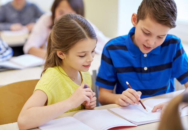 educação, ensino fundamental, aprendizagem e conceito de pessoas - grupo de crianças da escola com canetas e cadernos escrevendo teste em sala de aula