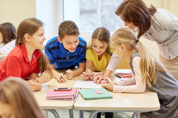 educação, ensino fundamental, aprendizagem e conceito de pessoas - professor ajudando crianças da escola escrevendo teste em sala de aula