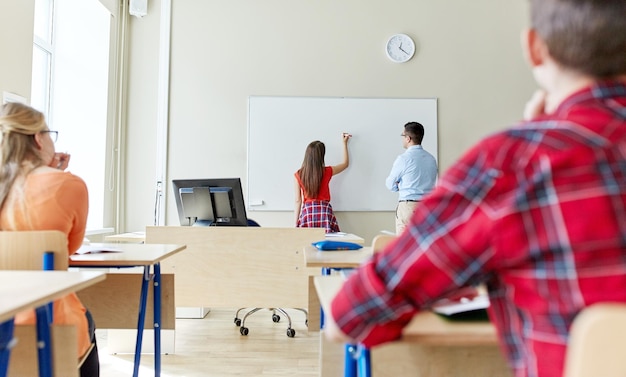 educação, ensino médio, aprendizagem e conceito de pessoas - aluna escrevendo algo no quadro branco em branco e professor em sala de aula