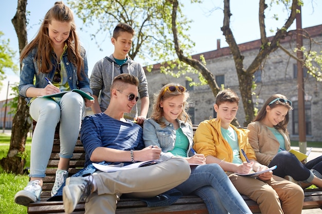 educação, ensino médio e conceito de pessoas - grupo de estudantes adolescentes felizes com notebooks aprendendo no pátio do campus