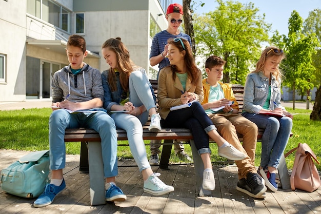 educação, ensino médio e conceito de pessoas - grupo de estudantes adolescentes felizes com notebooks aprendendo no pátio do campus