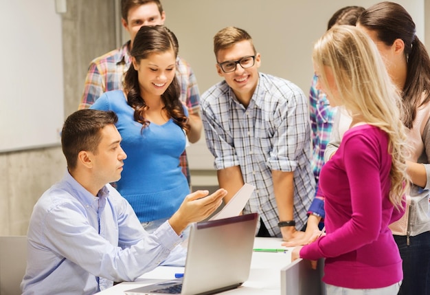 educação, ensino médio, tecnologia e conceito de pessoas - grupo de alunos sorridentes e professor com papéis, computador portátil em sala de aula