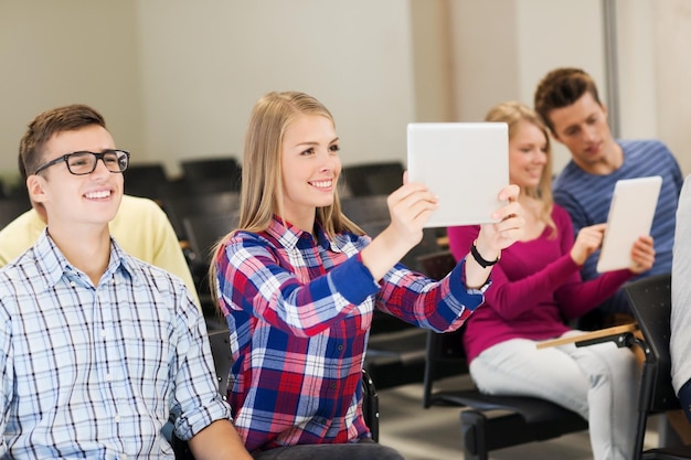 educação, ensino médio, trabalho em equipe e conceito de pessoas - grupo de estudantes sorridentes com computadores tablet pc fazendo foto ou vídeo na sala de aula