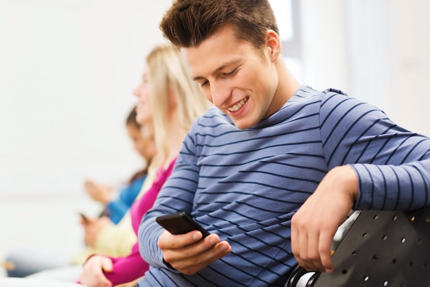 educação, ensino médio, trabalho em equipe e conceito de pessoas - grupo de estudantes sorridentes com smartphone na sala de aula