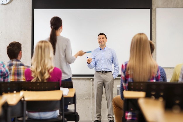 educação, ensino médio, trabalho em equipe e conceito de pessoas - professor sorridente em frente ao quadro branco e alunos em sala de aula