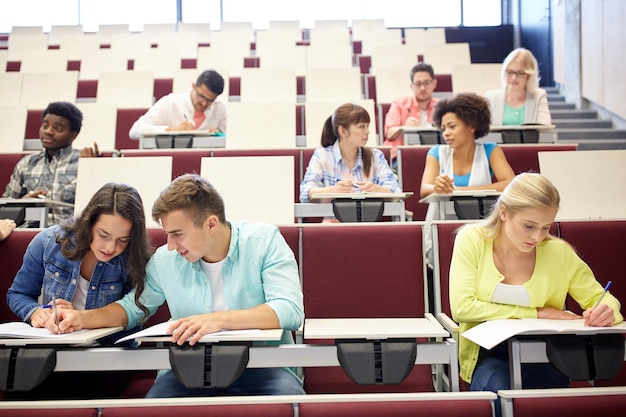 educação, ensino médio, universidade, aprendizagem e conceito de pessoas - grupo de estudantes internacionais com cadernos escrevendo na sala de aula