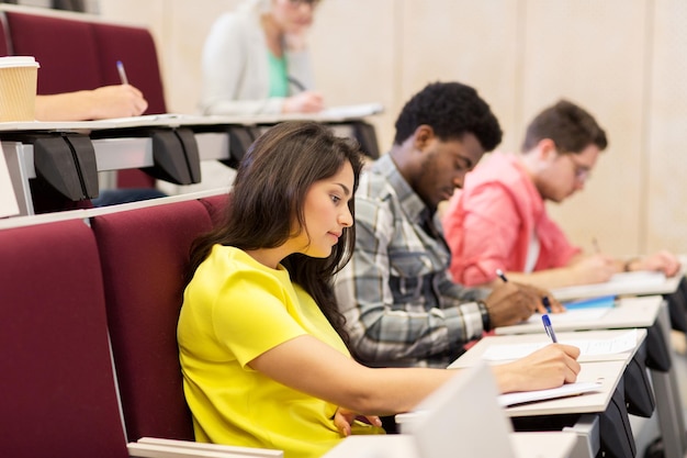 educação, ensino médio, universidade, aprendizagem e conceito de pessoas - grupo de estudantes internacionais com cadernos escrevendo na sala de aula