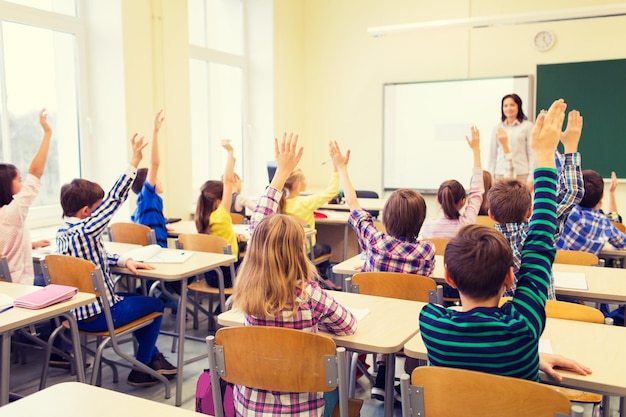 educação, escola primária, aprendizagem e conceito de pessoas - grupo de crianças da escola com professor sentado na sala de aula e levantando as mãos