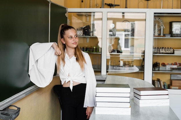 Educação escolar aluna com muitos livros posando no quadro-negro na sala de aula menina estudando na escola e se preparando para exames