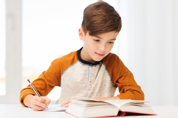 educação, infância, pessoas, lição de casa e conceito de escola - aluno com livro escrevendo para notebook em casa