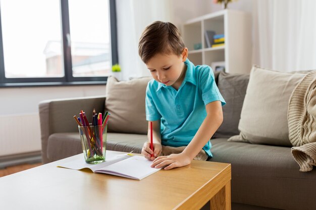 Educação infantil lazer e pessoas conceito menino feliz com caderno e lápis desenho em casa