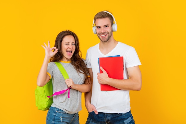 Educação moderna. dia do conhecimento. cara e menina seguram o caderno. estudantes universitários em fundo amarelo. estudar com pasta de trabalho. OK. casal alegre em fones de ouvido e mochila. de volta à escola.