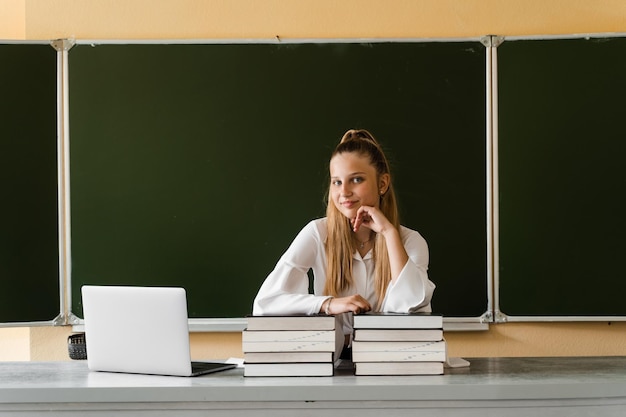 Educação na escola Estudante com laptop e muitos livros fazendo lição de casa Garota deitada em livros no conselho escolar estuda e estuda on-line