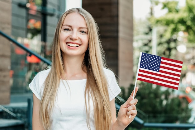 Educação no exterior. Menina jovem estudante sorrindo e mostrando uma pequena bandeira americana no contexto da universidade