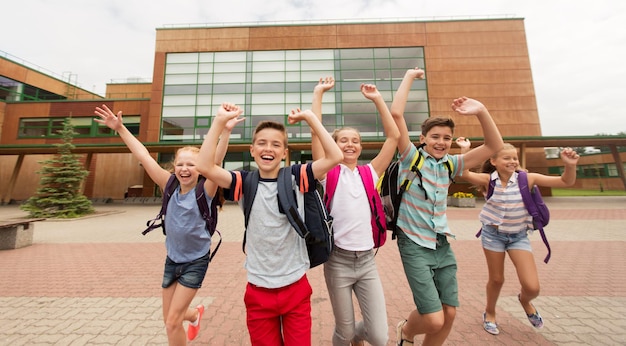 Foto educação primária, amizade, infância e conceito de pessoas - grupo de alunos felizes do ensino fundamental com mochilas correndo e acenando com as mãos ao ar livre