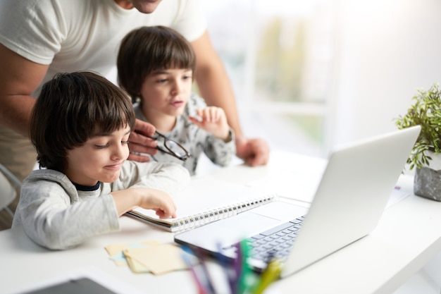 Educação primeiro. Foto recortada do pai observando os filhos enquanto eles têm aula on-line. Meninos latinos olhando para a tela do laptop, sentados juntos à mesa em casa