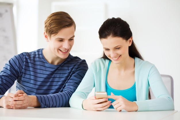 educação, relacionamentos e conceito de tecnologia - dois alunos sorridentes com smartphone na escola