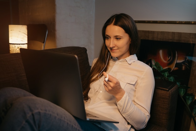 Foto educação remota. uma mulher caucasiana com fones de ouvido, estudando remotamente em seu laptop. uma empresária feliz trabalhando no sofá.