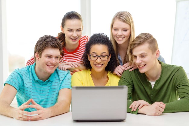 educação, tecnologia e conceito de faculdade - cinco estudantes sorridentes olhando para laptop na escola