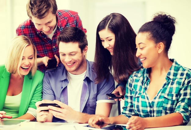 educação, tecnologia e internet - alunos sorridentes olhando para um smartphone na escola