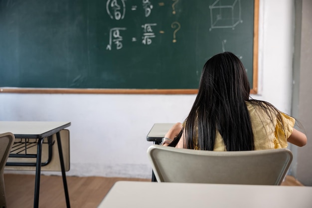 Educação. Vista traseira da menina da escola na aula na sala de aula escreve trabalhadora no quadro-negro, a criança primária está sentada na mesa na escola escrevendo ou desenhando no caderno, conceito de volta à escola