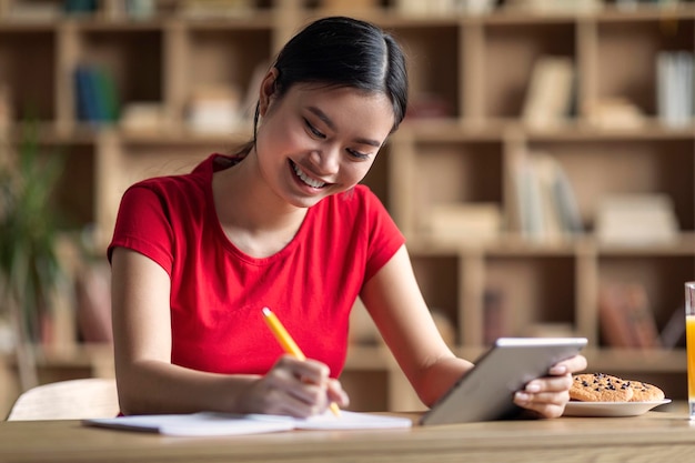 Educación en casa y nueva aplicación Alegre joven estudiante asiática haciendo la tarea con tableta ver lección en línea