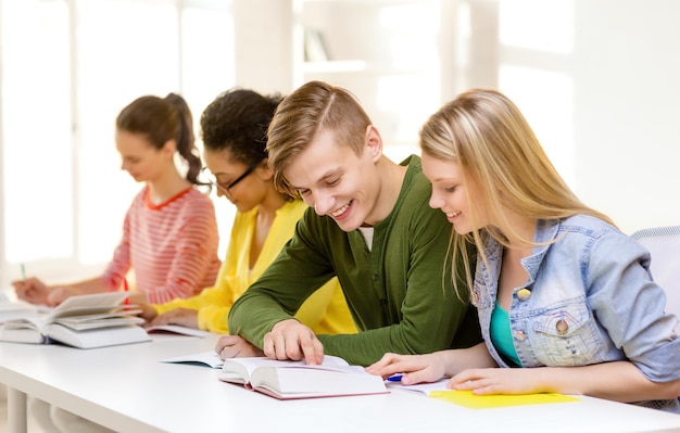 educación y concepto escolar - cinco estudiantes sonrientes con libros de texto y libros en la escuela