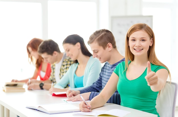 educación y concepto escolar - estudiantes sonrientes con libros de texto y libros y una chica al frente mostrando los pulgares hacia arriba en la escuela