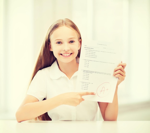 educación y concepto escolar - niña estudiante con prueba y grado A en la escuela