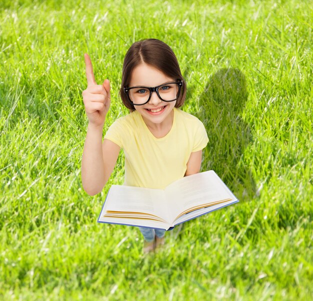 educación y concepto escolar - niña estudiante sonriente en anteojos con libro y dedo arriba