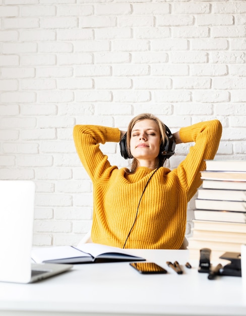 La educación a distancia. Aprendizaje electrónico. Mujer joven en auriculares negros sentado en el escritorio relajante después de un largo estudio