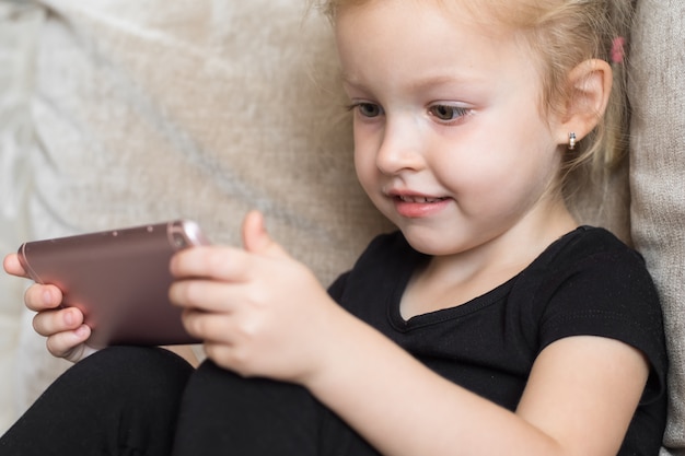 Educación a distancia, educación en línea para niños. Chica feliz con smartphone en manos. Niño viendo dibujos animados en línea, adicción a la computadora para niños, control parental.