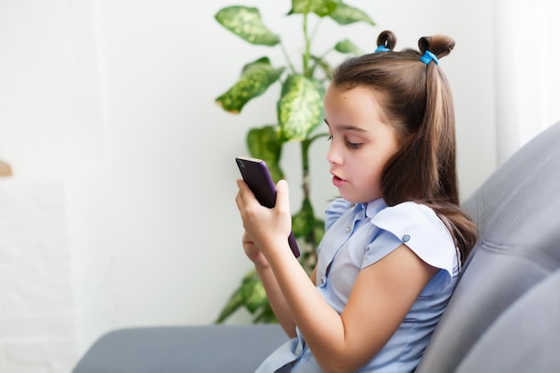 Educación a distancia, educación en línea para niños. Niña estudiando en casa frente al teléfono inteligente. Niño viendo dibujos animados en línea, adicción a la computadora para niños, control parental. Cuarentena en casa