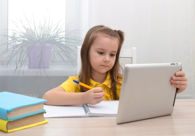 Educación a distancia en el hogar en línea. Una colegiala está estudiando con una tableta digital y haciendo los deberes escolares. Estudie libros y cuadernos sobre la mesa.