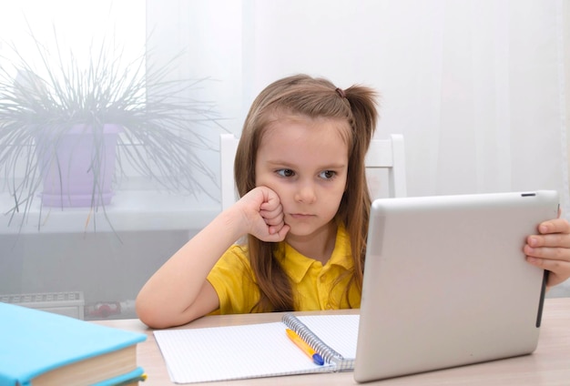 Educación a distancia en el hogar en línea. Una colegiala está estudiando con una tableta digital y haciendo los deberes escolares. Estudie libros y cuadernos sobre la mesa.